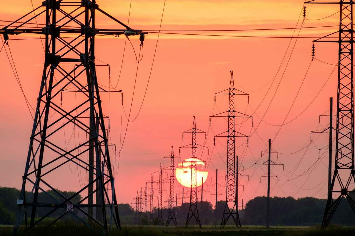 black transmission towers of power grid in front of orange-red sunset